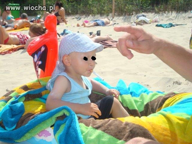Dziecko z papierosem na plaży, obok rodzice
