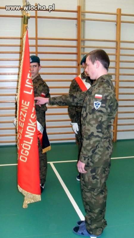 "Kadet" w mundurze i klapkach ślubujący na sztandar 